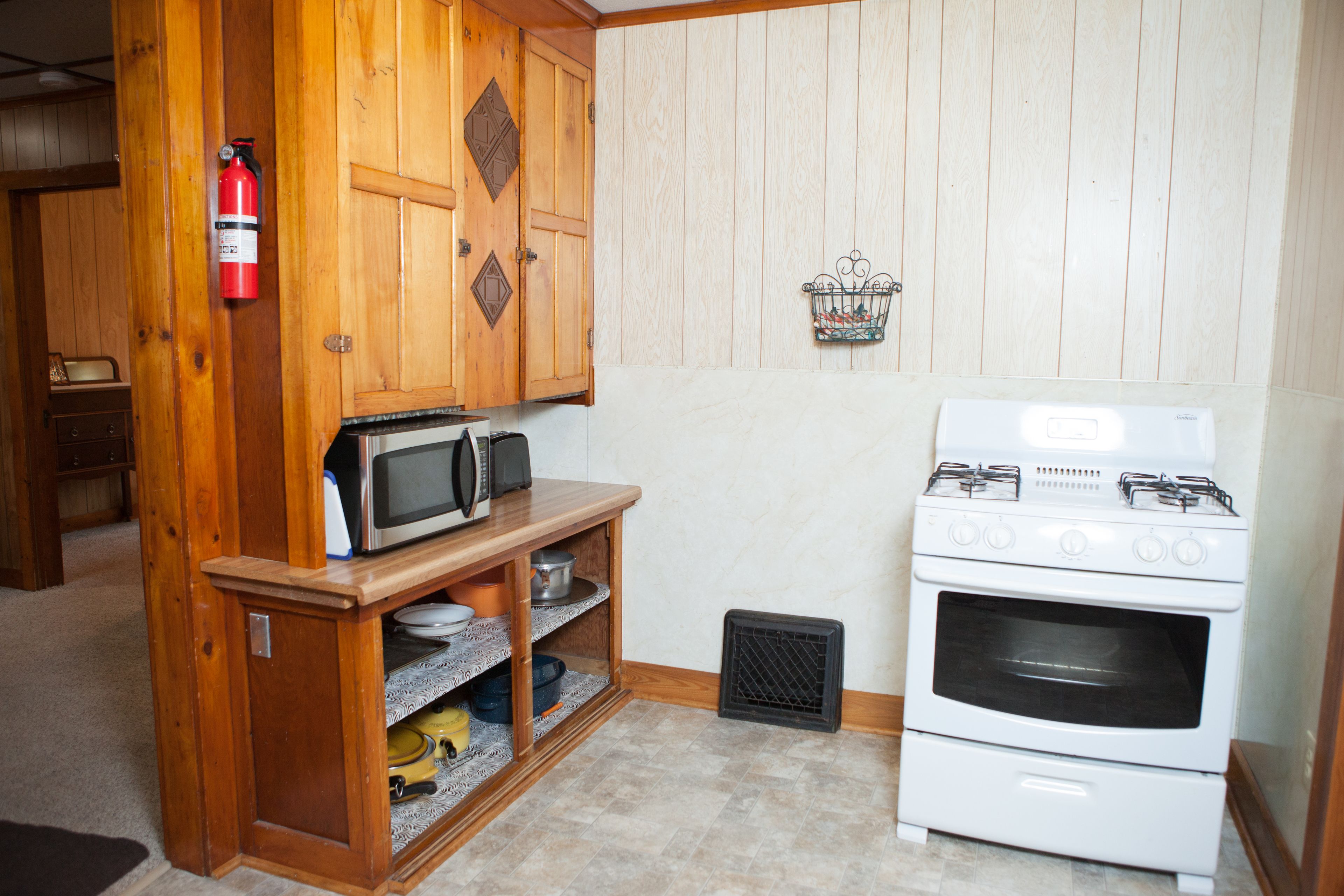 A compact kitchen with wooden cabinets, a microwave, a stove, and a small sink.