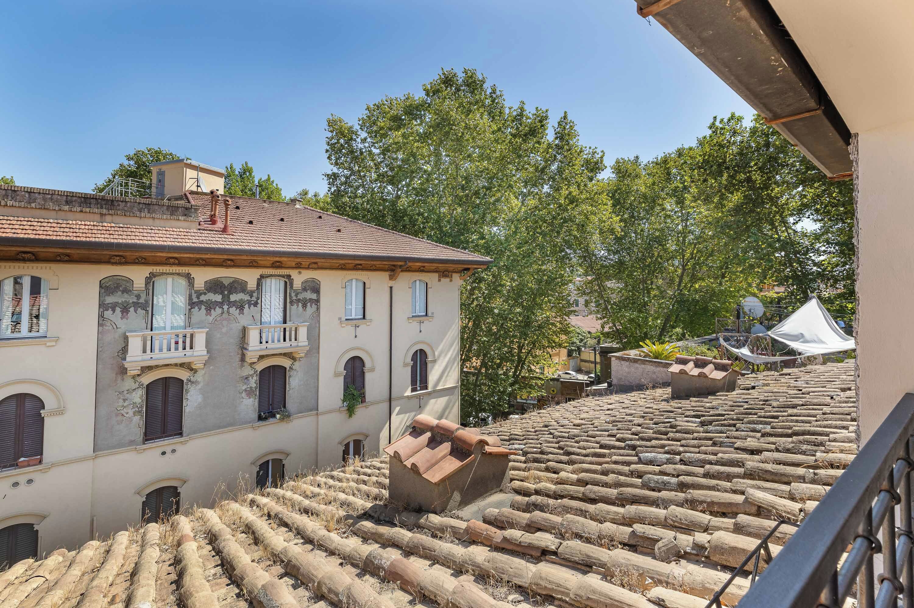 Um edifício com várias janelas e telhado de telhas, cercado por árvores e outras construções.