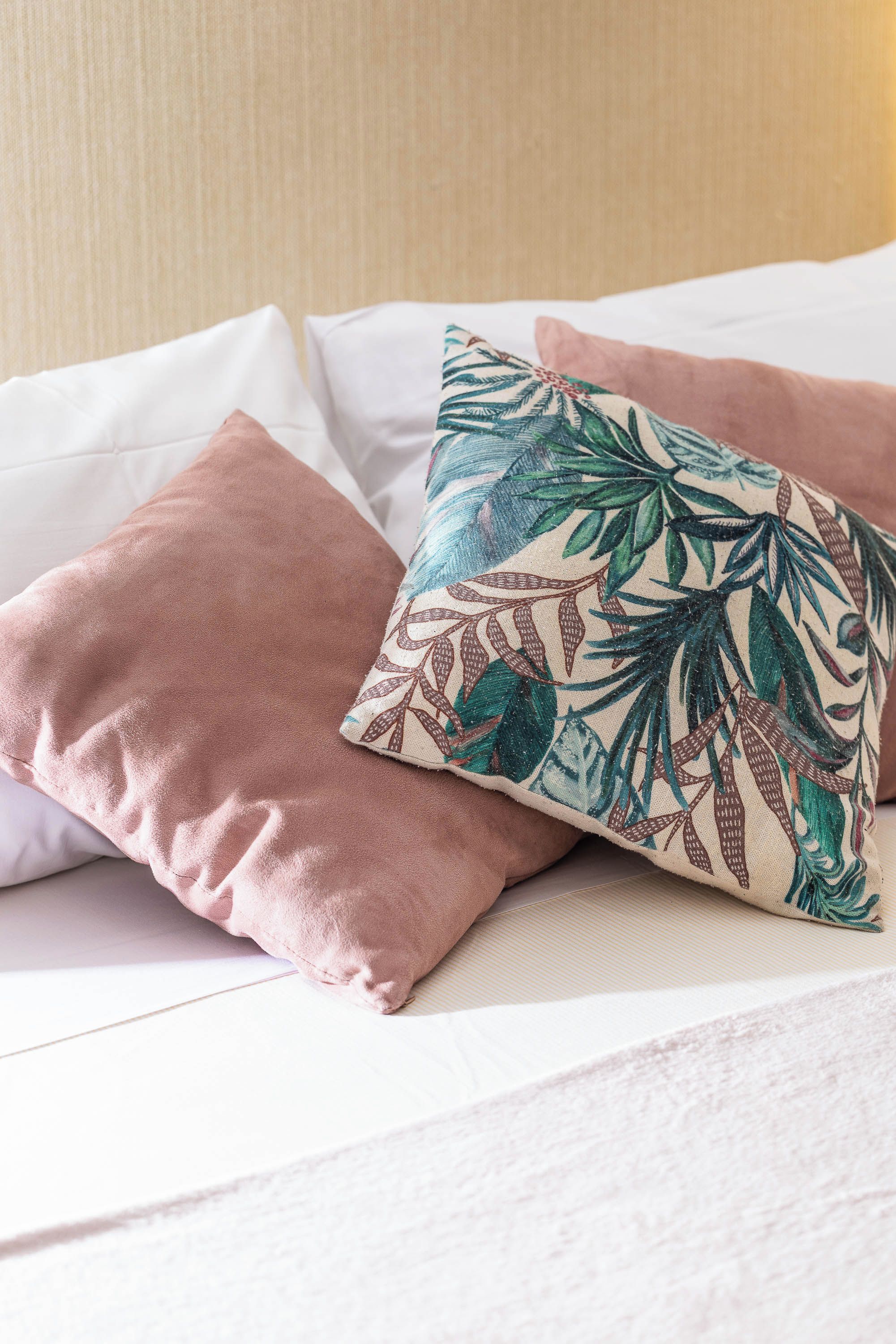 Cama com vários travesseiros, incluindo um com padrão floral e um rosa liso.