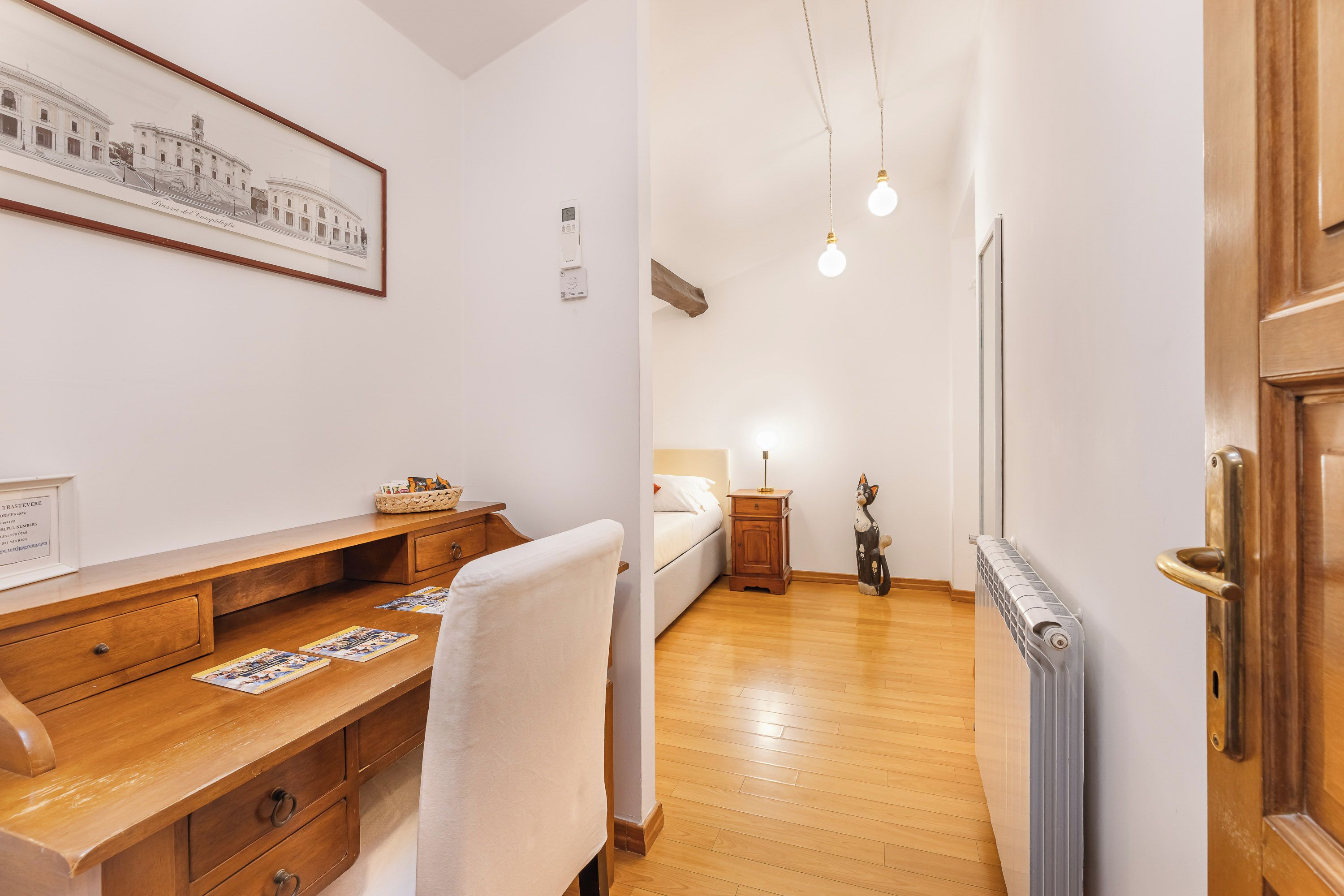 Una habitación con un escritorio de madera, una cama, un radiador y una puerta.