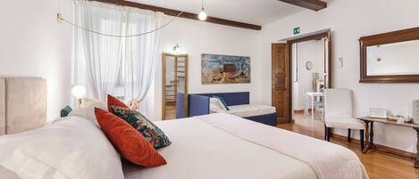 Une chambre d’hôtel avec un lit, un bureau, une chaise, un tableau et une porte donnant sur une autre pièce.