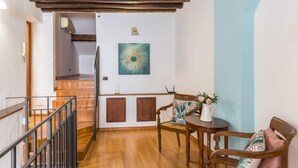 A staircase with wooden steps and a metal railing, leading to a room with a wooden floor, a table with chairs, and a wall-mounted air conditioning unit. - Torripa Group - Trastevere (Rome)