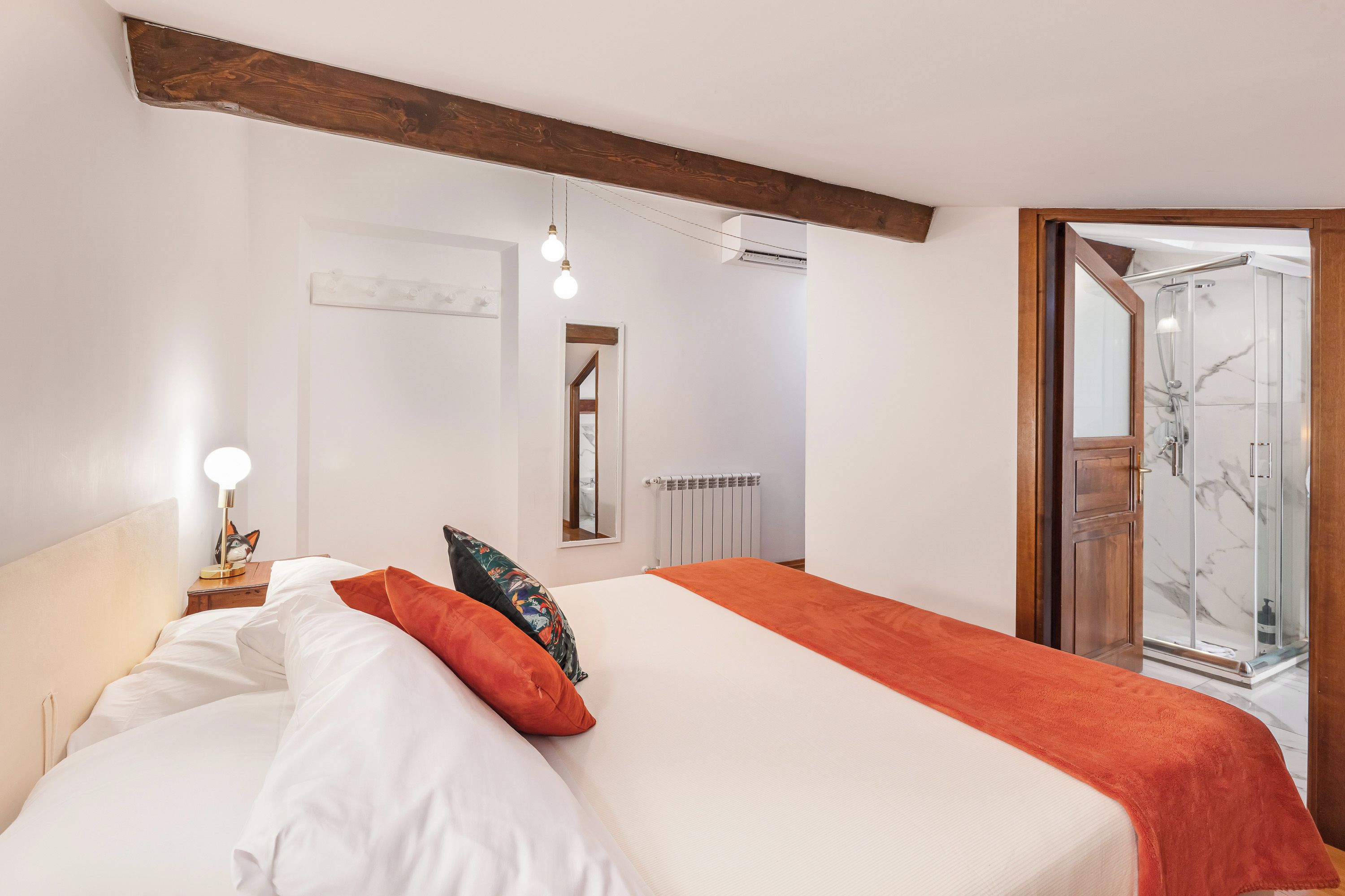 A hotel room with a bed, a nightstand, a lamp, a mirror, and a shower area.