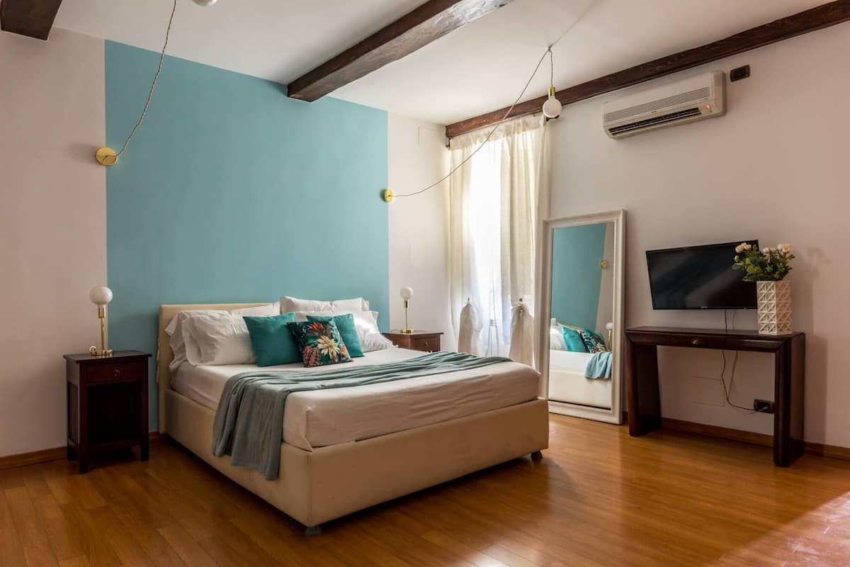A bedroom with a bed, bedside tables, a TV, and an air conditioning unit.