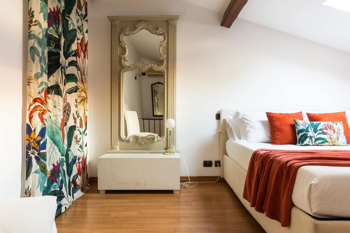 A bedroom with a bed, a nightstand, a mirror, and a window.