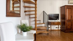 A staircase with a wooden finish, a white sofa, a small table with a plant, a TV on a wooden stand, and a wooden cabinet. - Torripa Group - Trastevere (Rome)