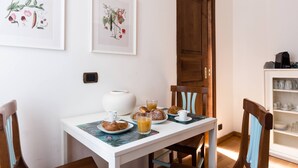 A breakfast setup with pastries, coffee, and juice on a table, framed botanical prints on the wall, and a cabinet with dishes. - Torripa Group - Trastevere (Rome)
