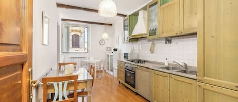 A kitchen with wooden cabinets, a dining table with chairs, a hanging light fixture, and a clock on the wall.