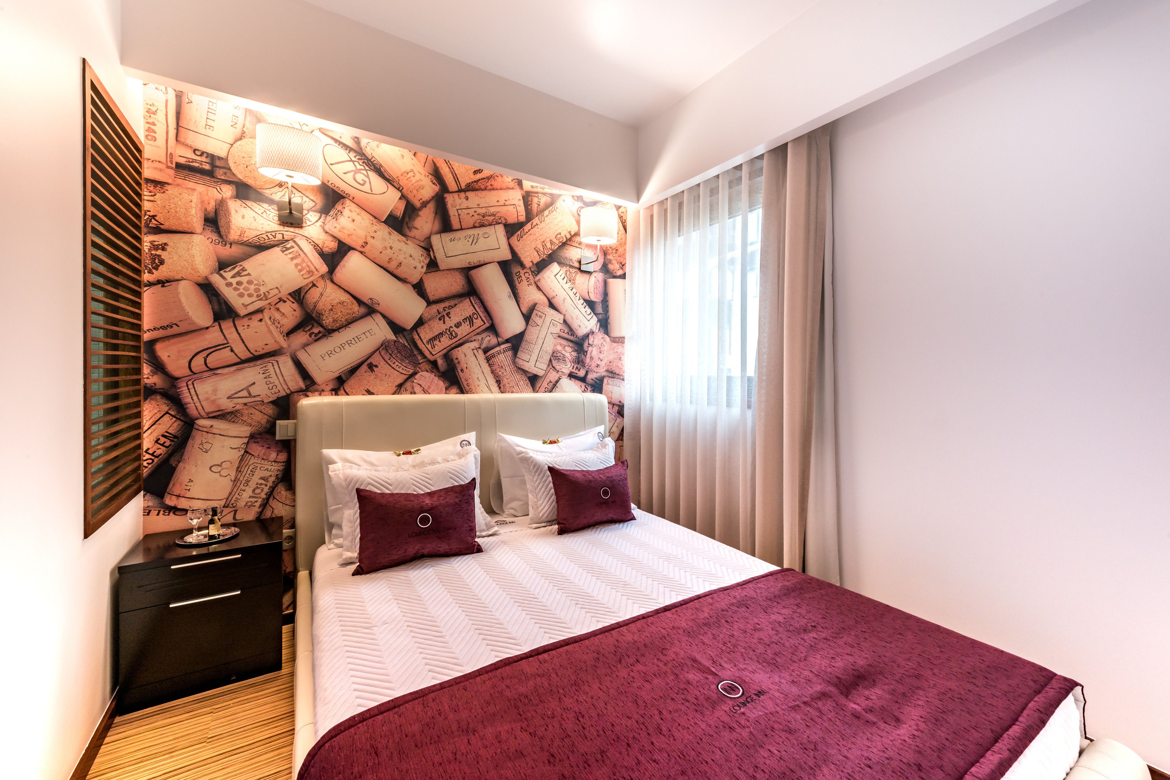 Een hotelkamer met een bed, nachtkastje, prikbord aan de muur en een raam met gordijnen.