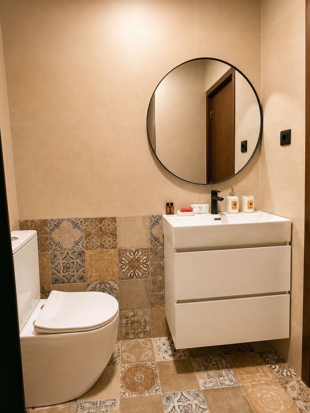 A bathroom with a toilet, a sink with a mirror, and patterned tiles on the walls and floor.