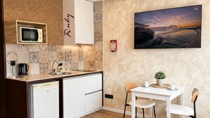 A compact kitchen with a microwave, sink, and cabinets, a dining area with a table and chairs, and a wall-mounted TV.