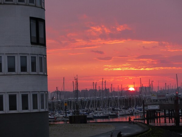 Een jachthaven met aangemeerde boten, een zonsondergang op de achtergrond en een gebouw met veel ramen.
