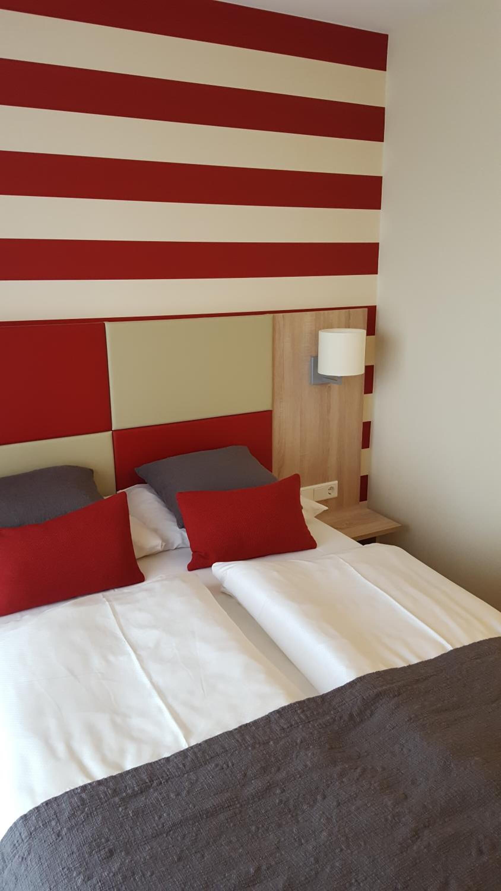 A hotel room with a bed, pillows, a nightstand, and a wall with a striped pattern.