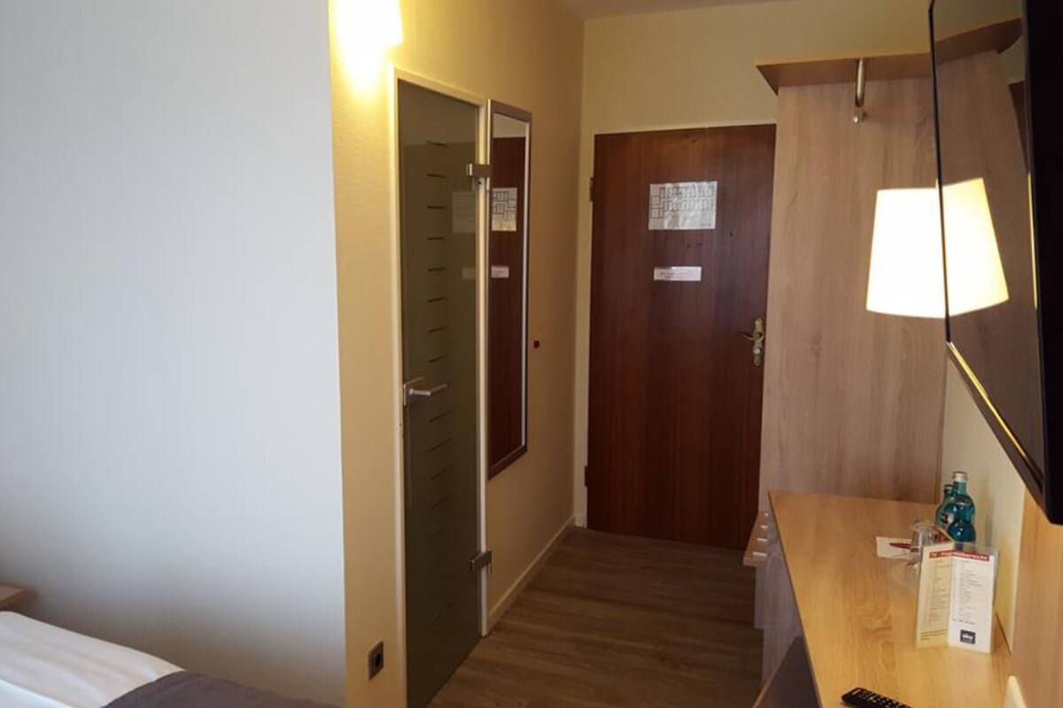 Une chambre d’hôtel avec un lit, un bureau avec une lampe, une armoire et une porte avec une pancarte.