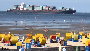 Een strand met gele strandhutten en een grote vrachtschip op de achtergrond.