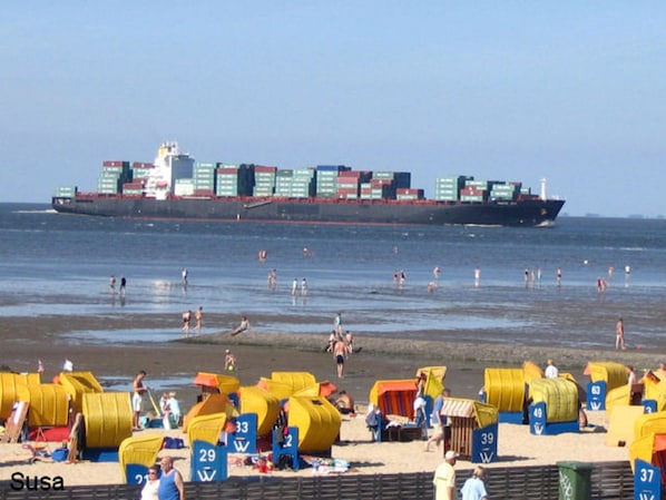 Une plage avec des cabanes de plage jaunes et, au loin, un grand cargo.