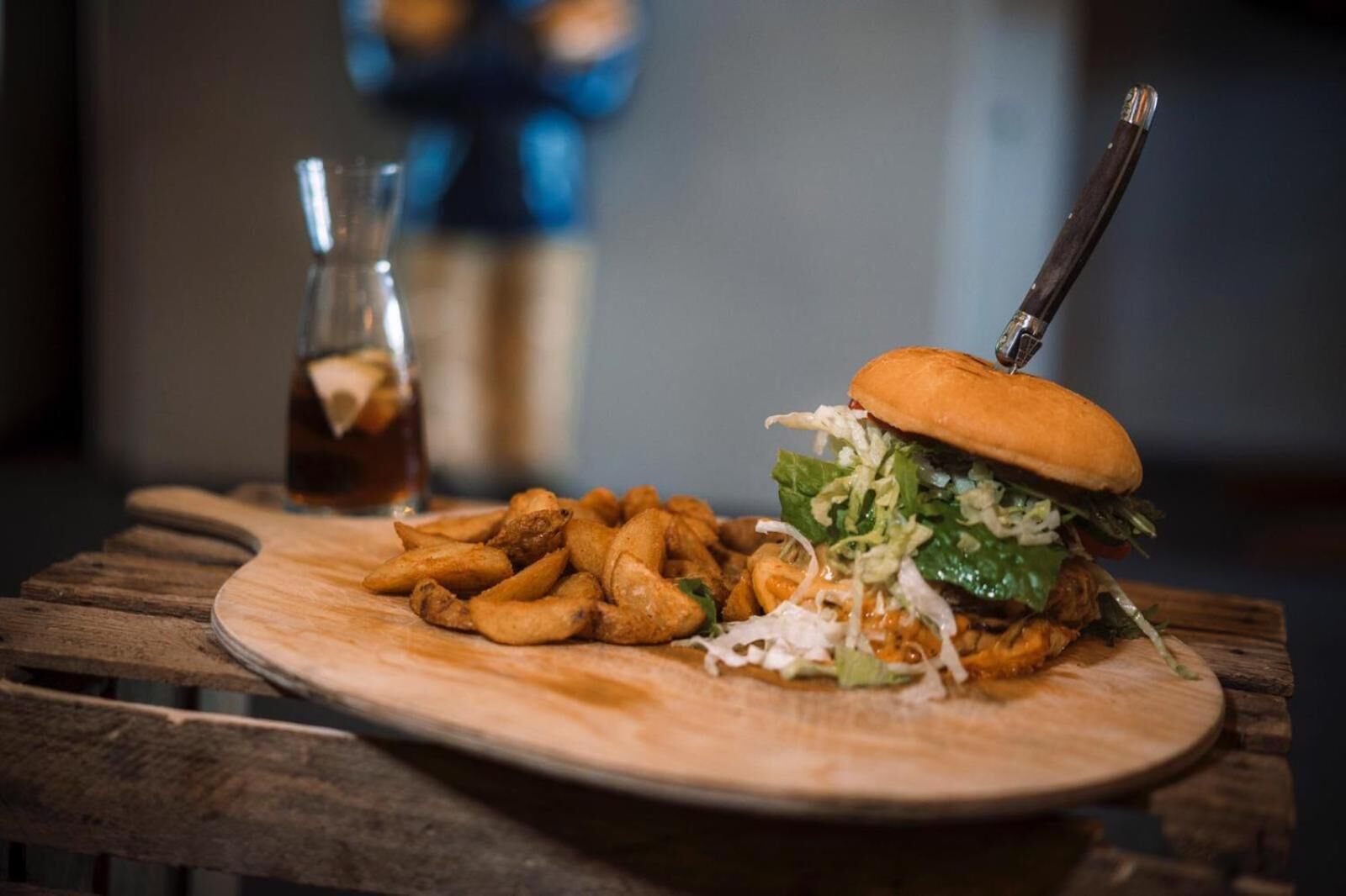 A wooden table with a plate of food, including a burger and fries, and a glass of a dark beverage.