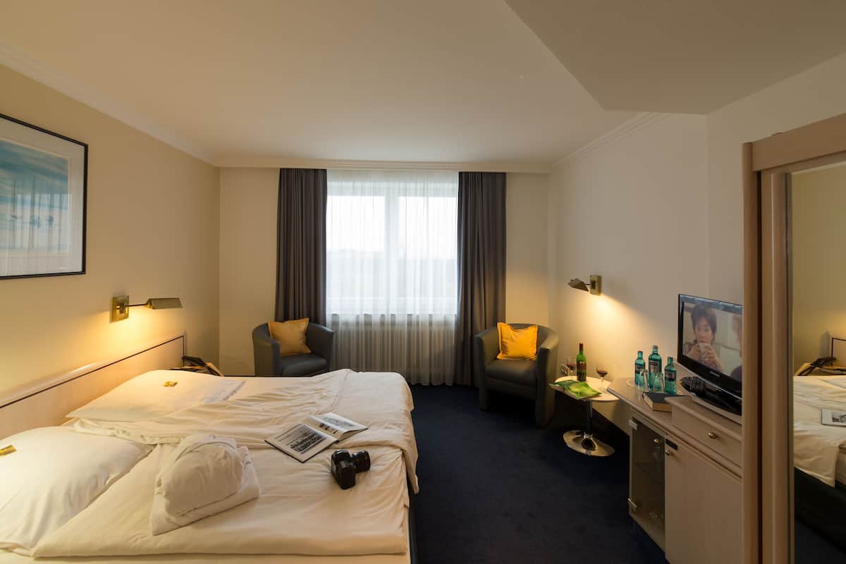 Une chambre d’hôtel avec deux lits, un bureau avec une télévision et une grande fenêtre avec des rideaux.