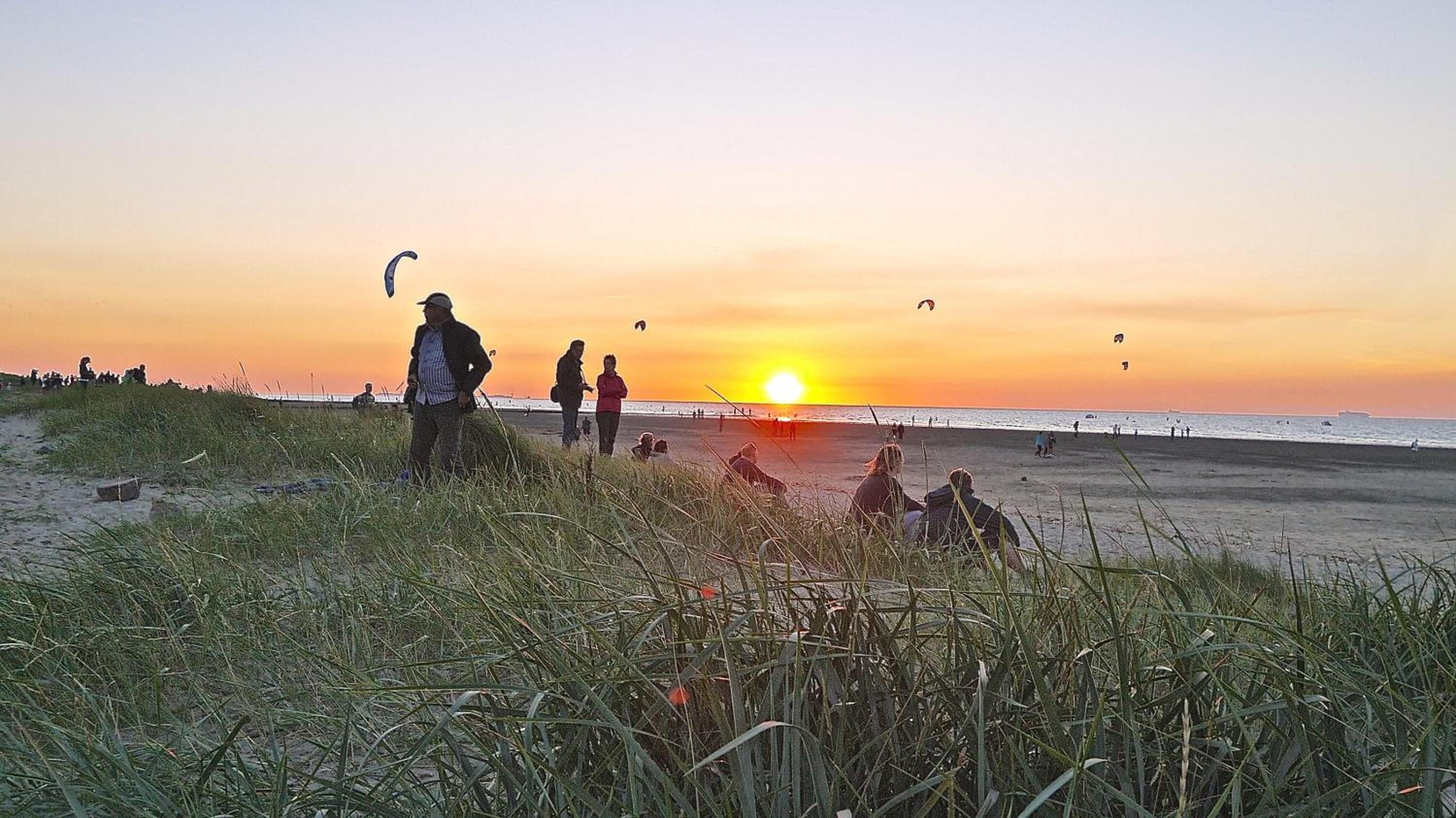 Scena di spiaggia al tramonto con persone e aquiloni.