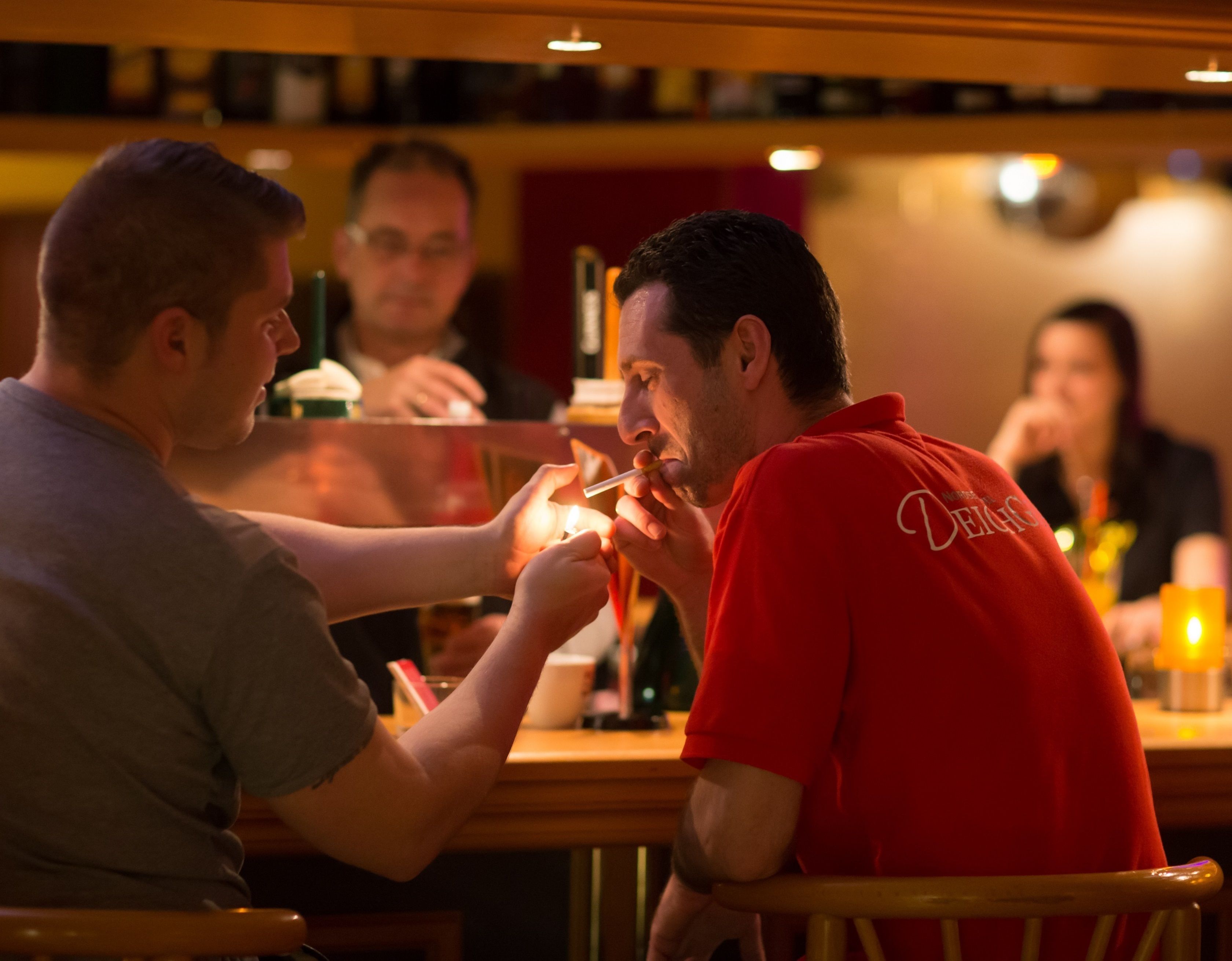 A person in a red shirt with a logo, seated at a table with another individual.