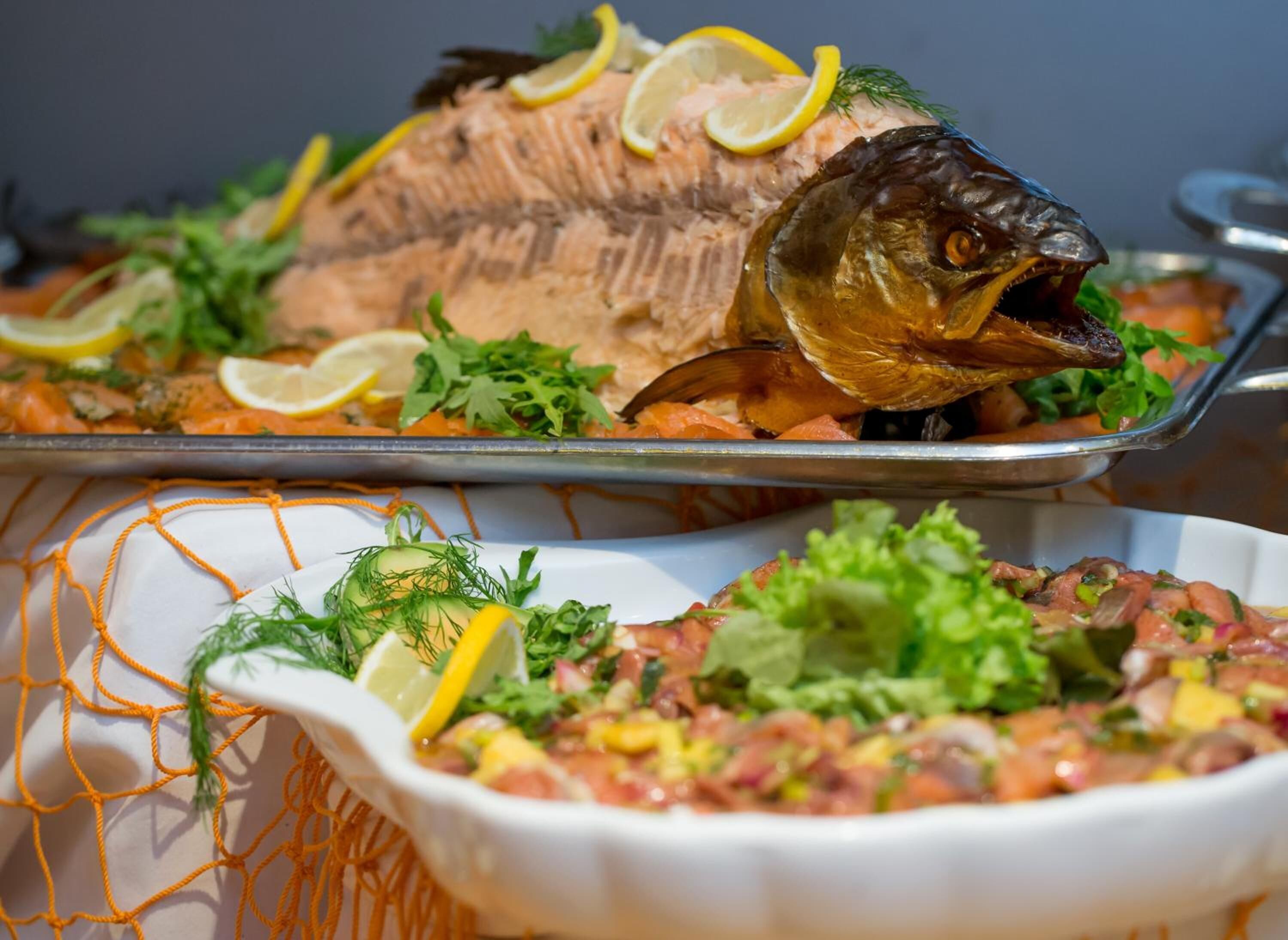 Ein Fischgericht, garniert mit Zitrone und Kräutern, sowie eine Salatschüssel mit ähnlichen Zutaten.