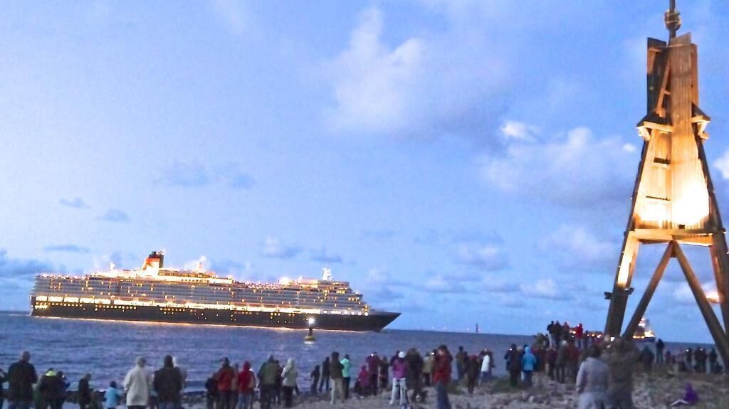 A large cruise ship docked at a port with a crowd of people on the shore.