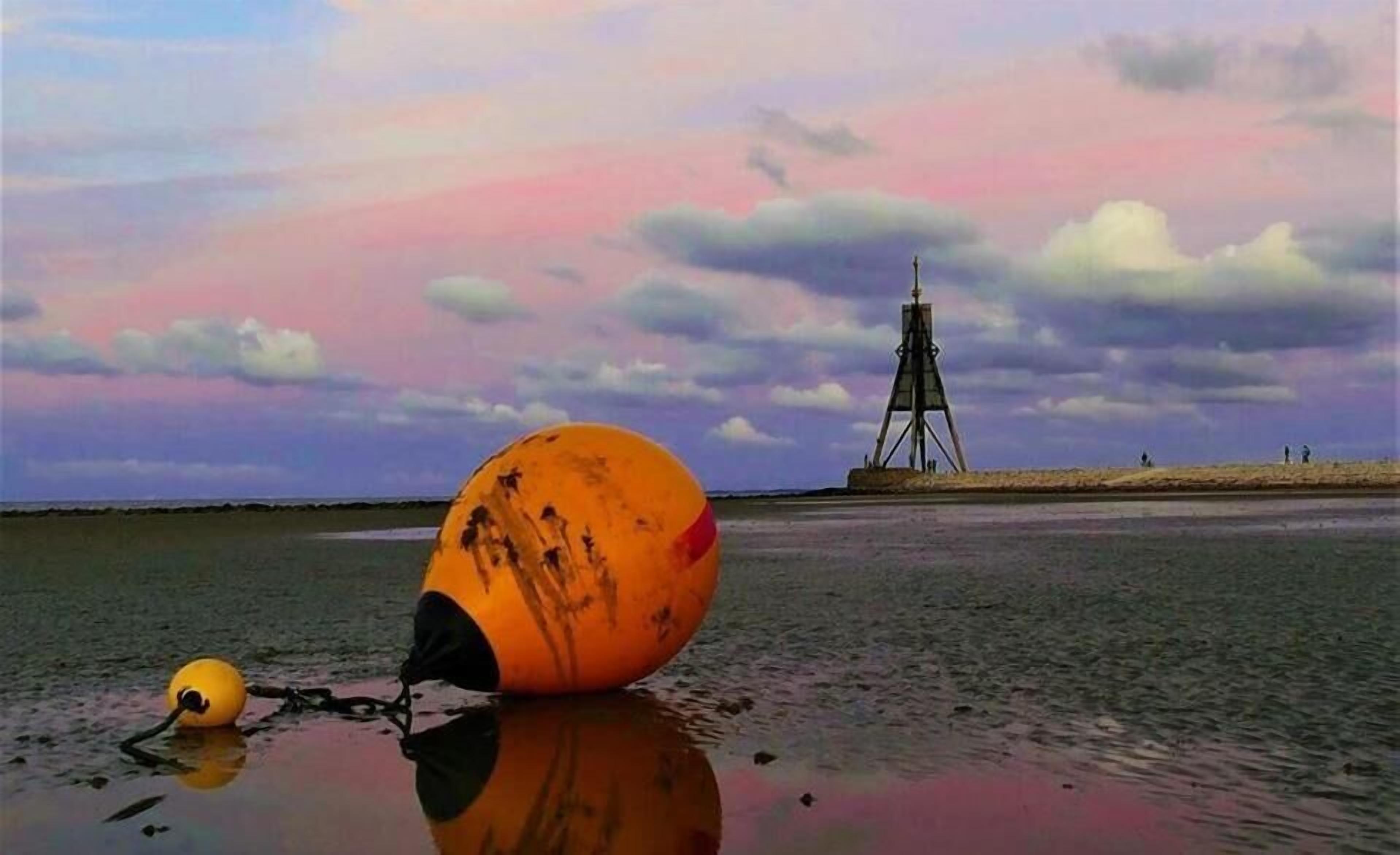 A buoy on a beach with a lighthouse in the background.