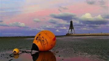 A buoy on a beach with a lighthouse in the background.