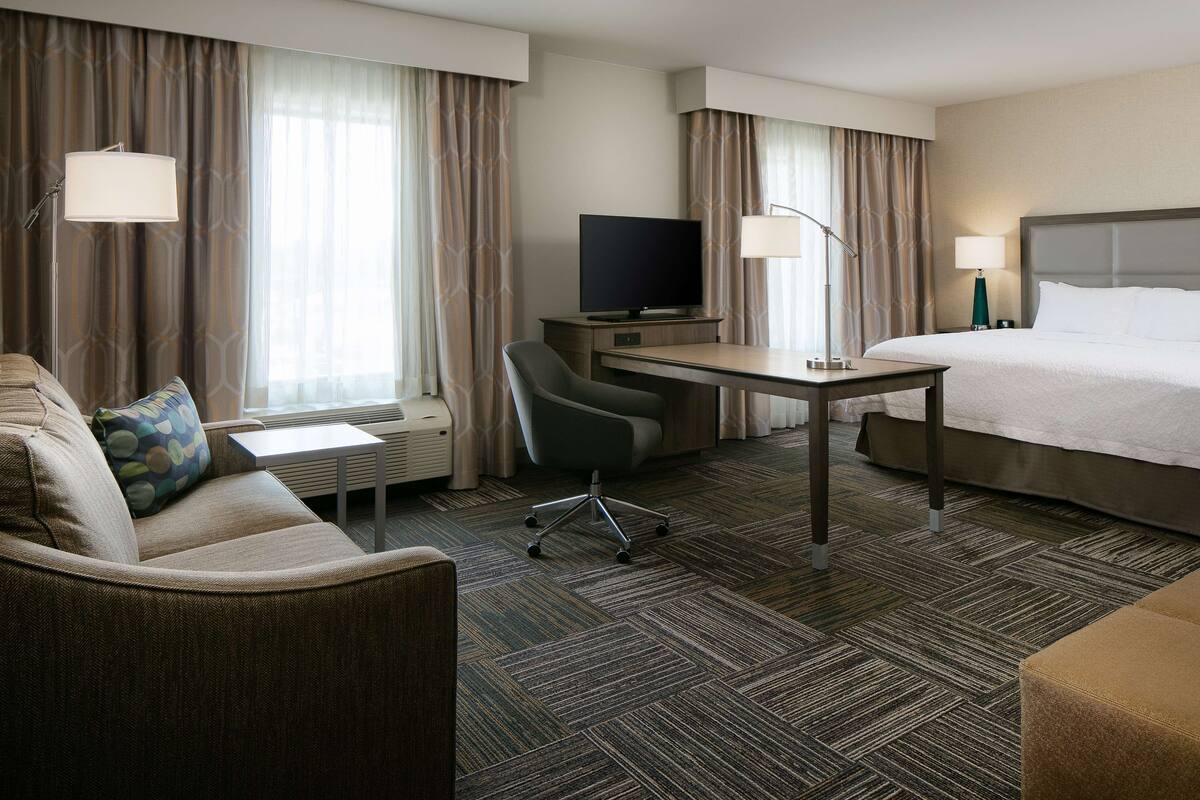 A hotel room with a bed, a desk, a chair, a television, and a window with curtains.