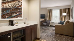 A hotel room with a kitchenette, a sofa, a TV, and a large window with curtains. - Hampton Inn & Suites Mason City (Mason City)