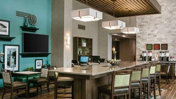 A modern hotel lobby with a central bar area, seating arrangements, and a television screen. - Hampton Inn & Suites Mason City (Mason City)
