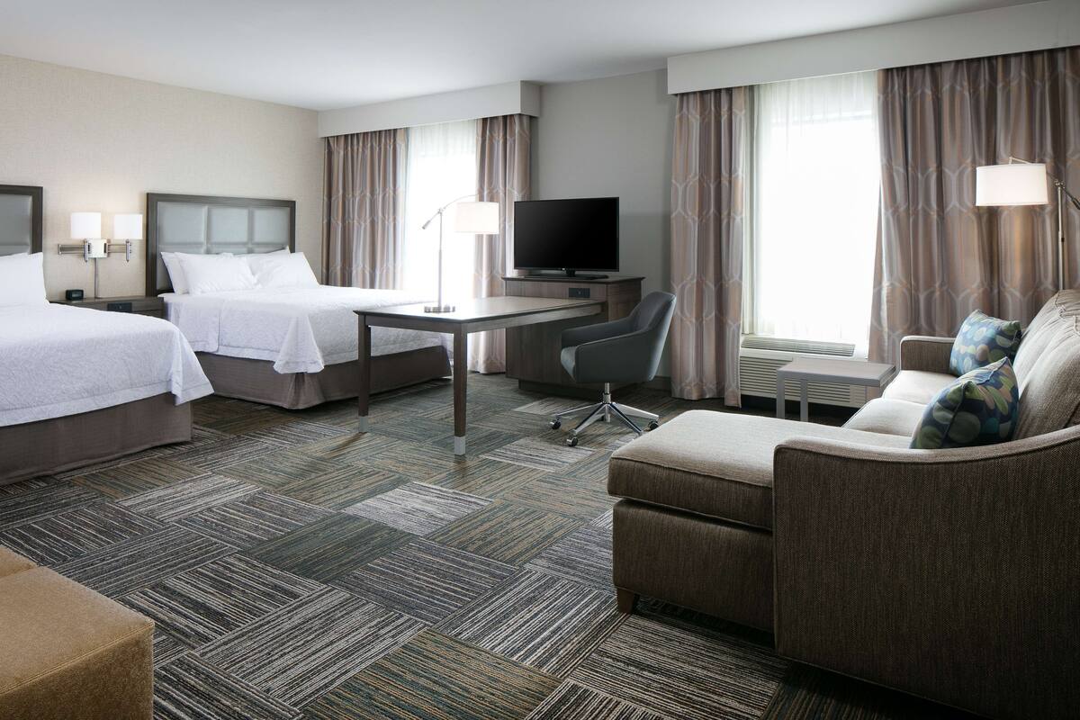 A hotel room with two beds, a desk, a television, a sofa, and a chair.