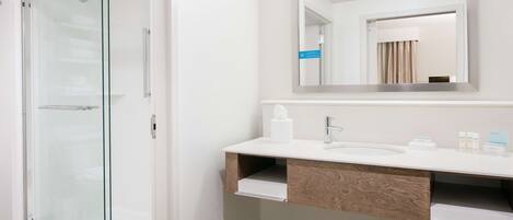 Un baño moderno con cabina de ducha de vidrio, un lavabo blanco y un espejo sobre el mueble.