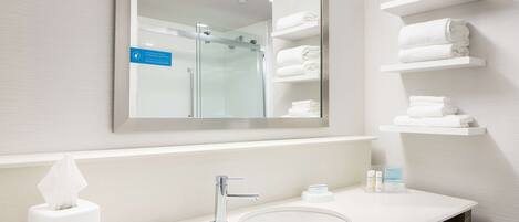 A modern bathroom with a large mirror, a sink, and shelves with folded towels.
