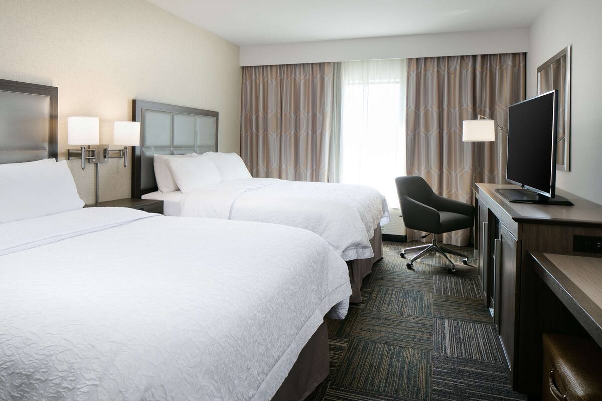 A hotel room with two beds, a desk with a television, and a chair.