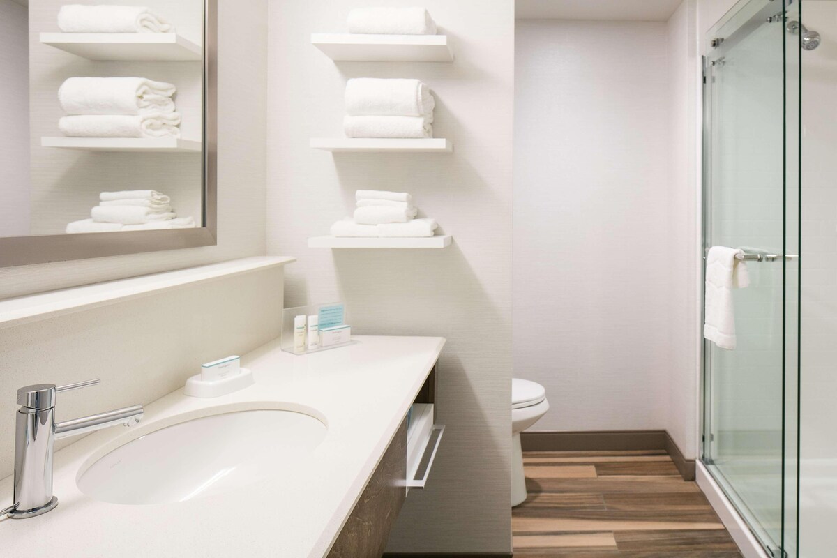 A modern bathroom with a large mirror, a sink, a glass shower enclosure, and towel racks.