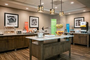 A modern kitchen with a central island, various food stations, and a coffee machine. - Hampton Inn & Suites Mason City (Mason City)