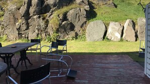 Une terrasse extérieure avec une table et des chaises, une plateforme en bois et, en arrière-plan, une colline rocheuse.
