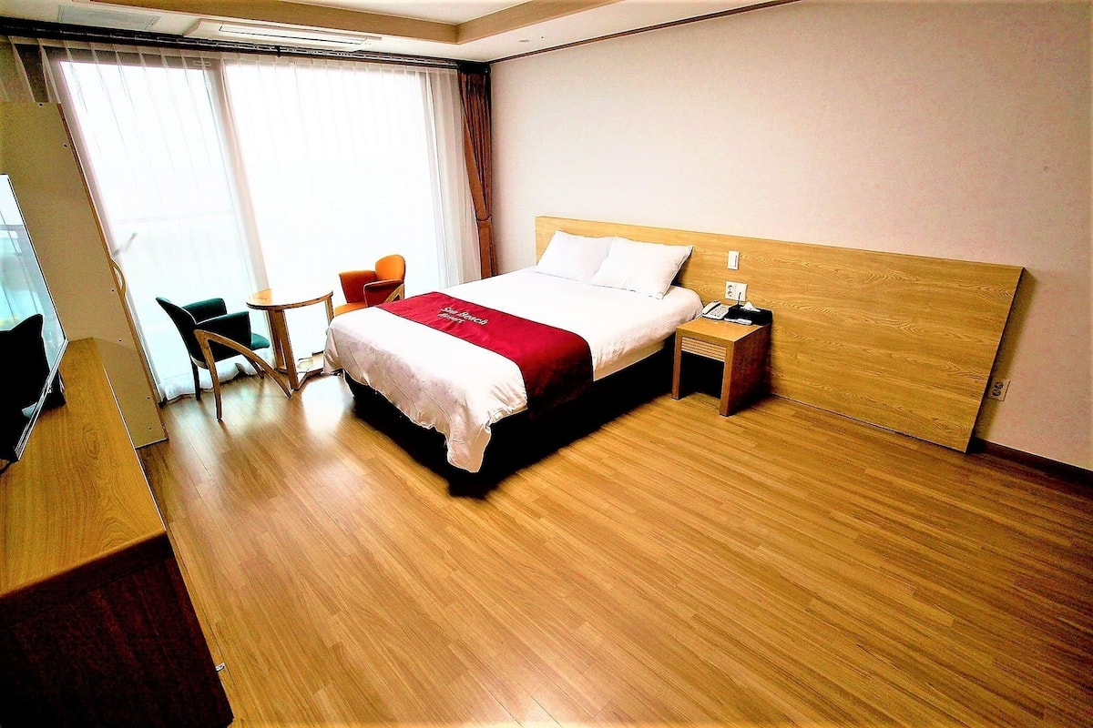 A hotel room with a wooden bed, a desk, a chair, and a small table.
