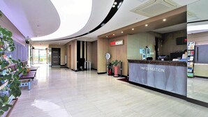 Un hall d’hôtel avec un comptoir d’accueil, une horloge et une plante.