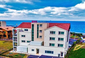 A multi-story hotel with a red roof, named "RESORT," featuring balconies, a central elevator shaft, and a parking lot. - Sunbeach Resort (Jeju City)
