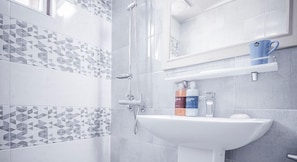 A modern bathroom with a shower, a sink, and a mirror. There are toiletries on the sink and a blue cup on the shelf. - Sunbeach Resort (Jeju City)