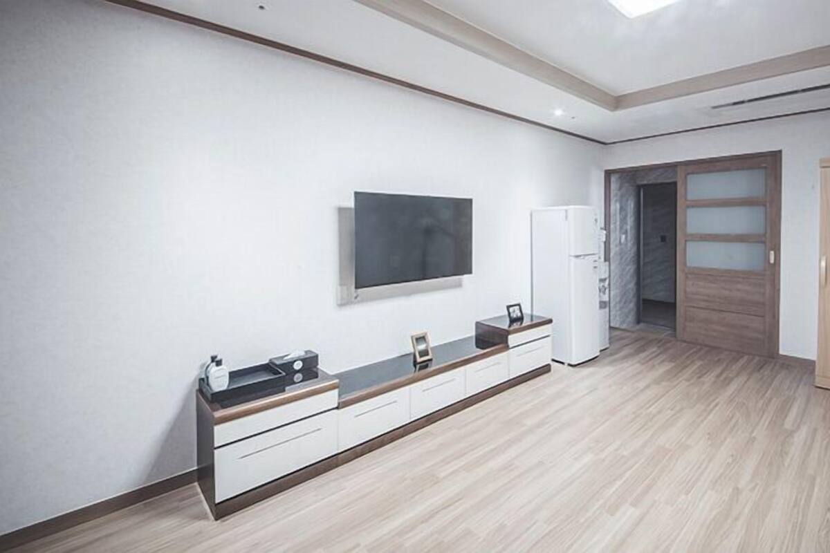 A modern, minimalist bedroom with a large bed, a built-in wardrobe, and a TV mounted on the wall.