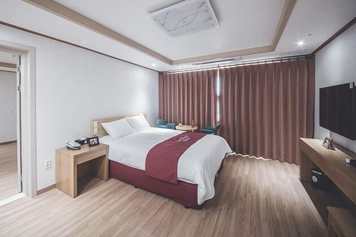 A modern hotel room with a bed, a desk, a TV, and a window with curtains.
