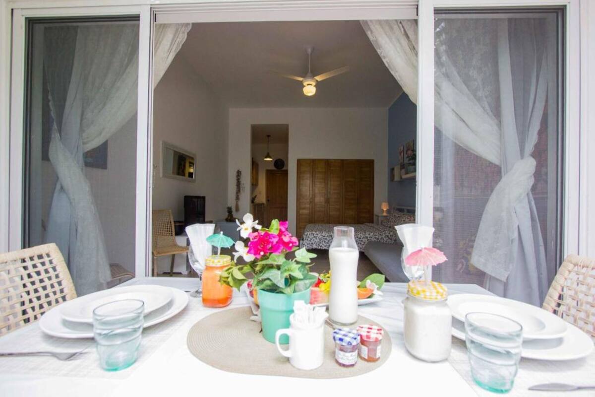 A dining area with a table set for two, featuring a pitcher of milk, a vase with flowers, and a pitcher of orange juice.