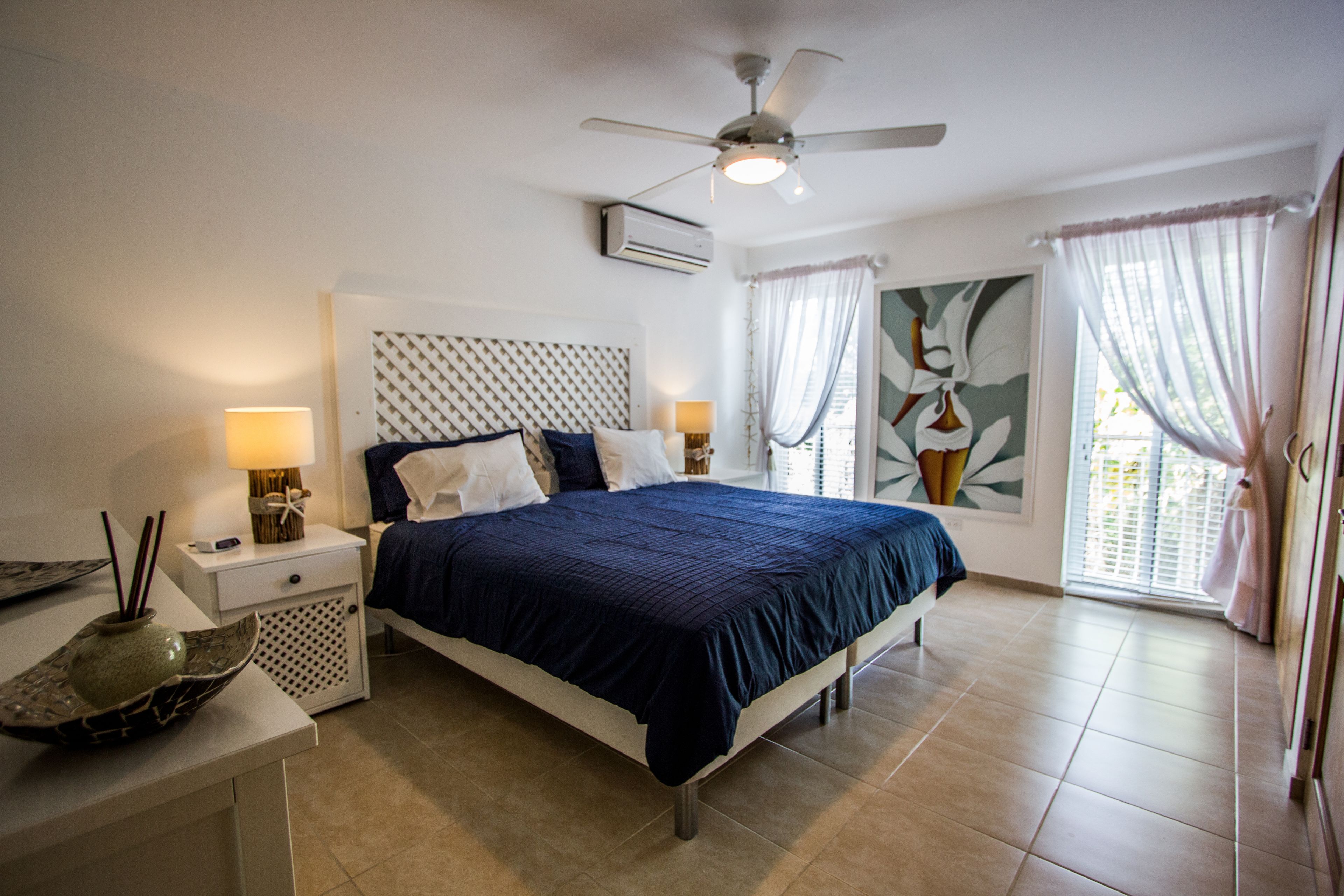 Une chambre à coucher avec un lit, des tables de chevet, un ventilateur de plafond et une fenêtre avec des rideaux.