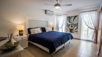 Une chambre à coucher avec un lit, des tables de chevet, un ventilateur de plafond et une fenêtre avec des rideaux.
