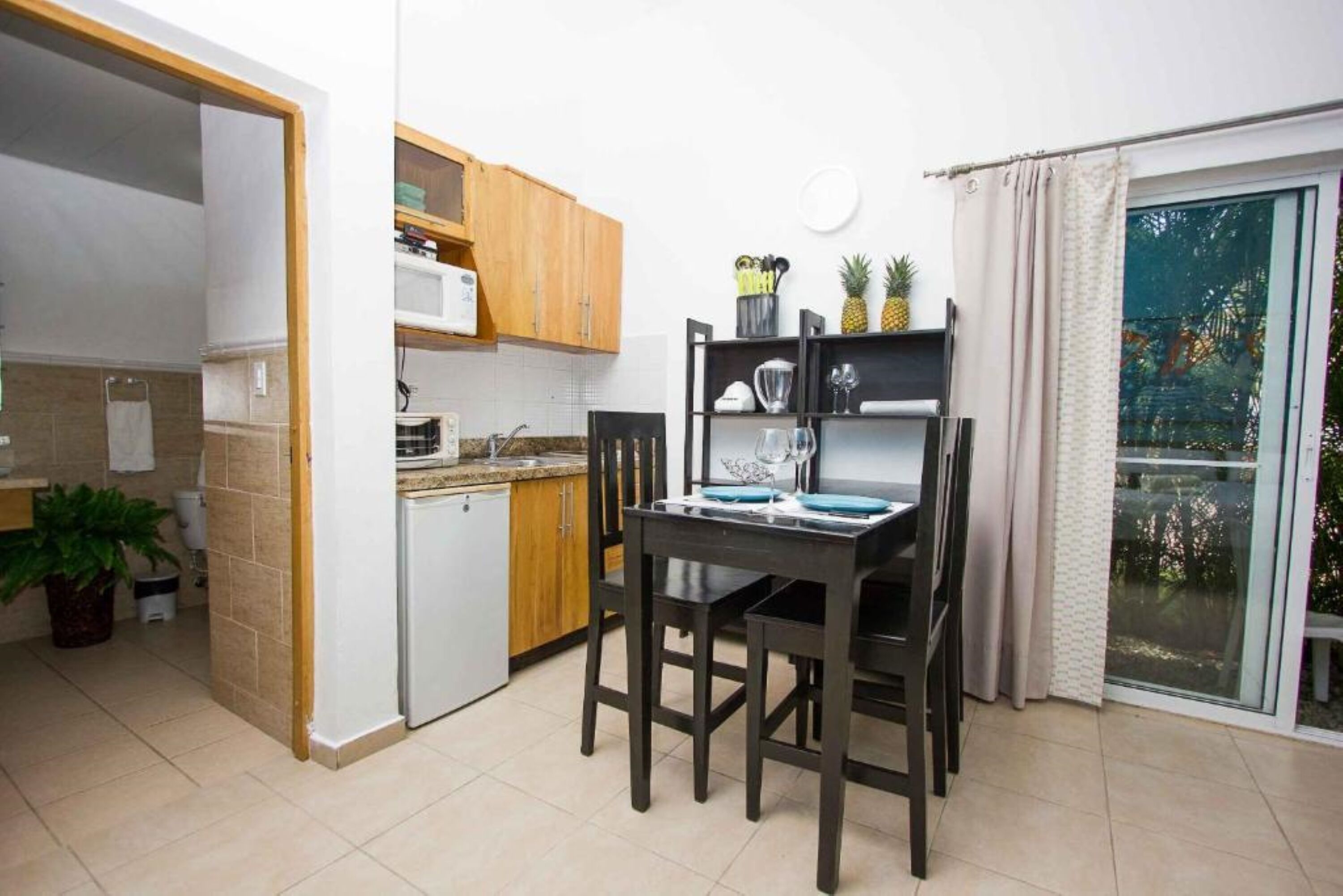 A compact kitchen with wooden cabinets, a small refrigerator, and a dining table with chairs.