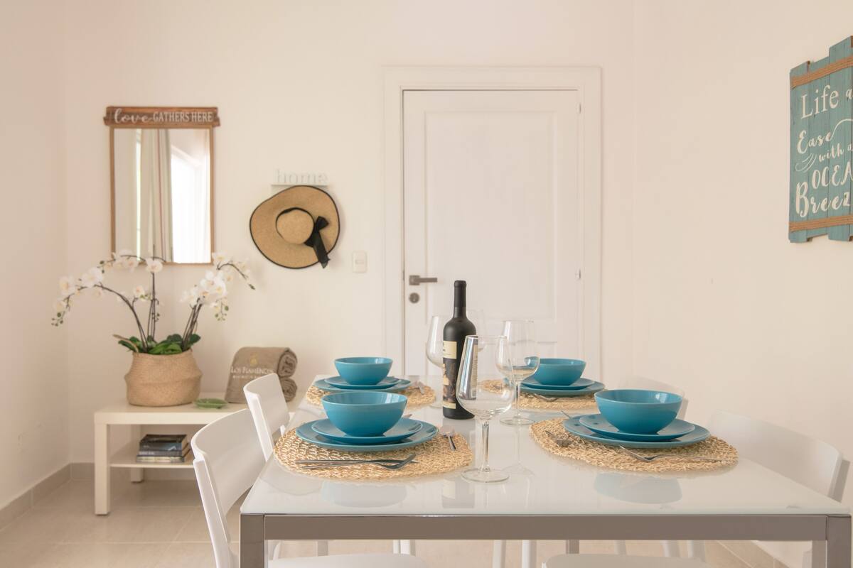 A dining table set with blue bowls and plates, a wine bottle, and a glass. There is a white door, a mirror, and a wall sign.