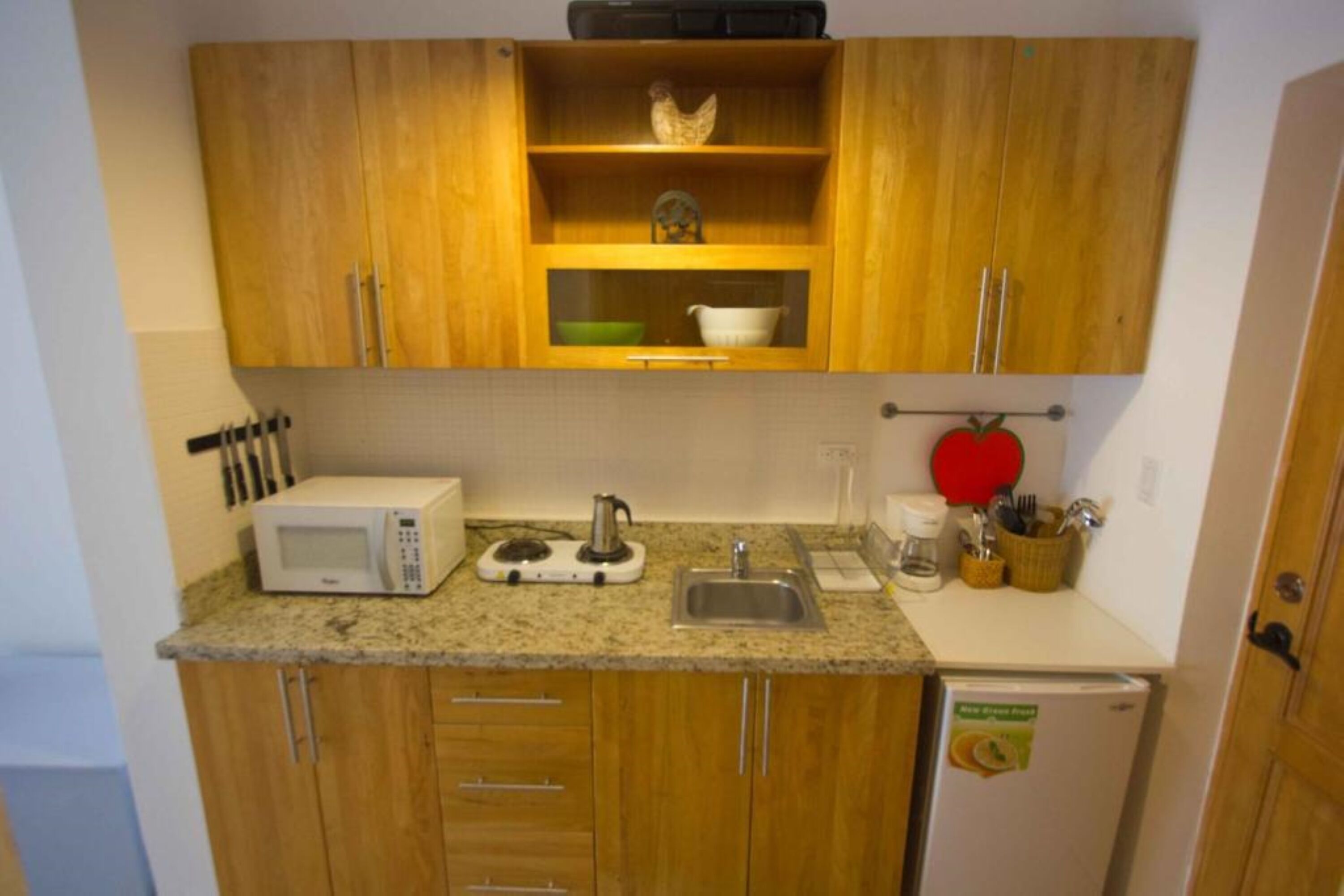 Eine kleine Küche mit Holzschränken, einer Mikrowelle, einem Wasserkocher, einem Spülbecken und einem kleinen Kühlschrank.